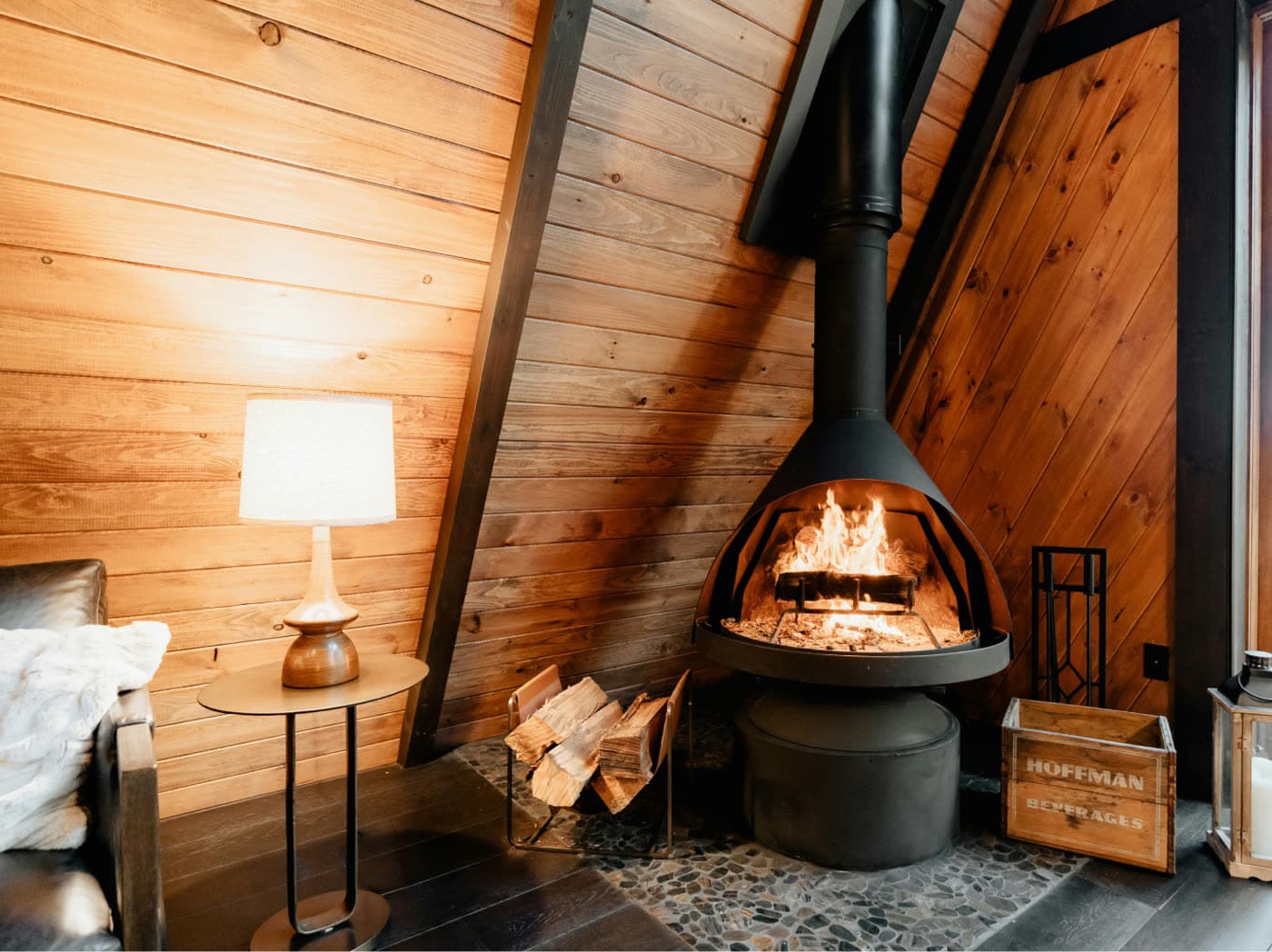 A black wood stove burning inside a wood-paneled A-frame cabin